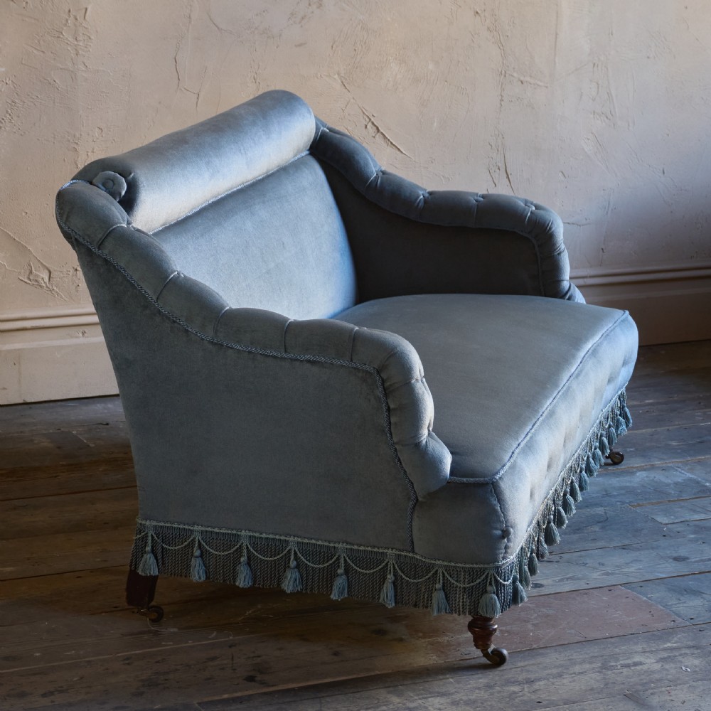 A Victorian bedroom settee upholstered in light blue velvet with buttoned details along the armrests and base, fitted with a tassel fringe skirt and turned wooden legs on castors. View IX