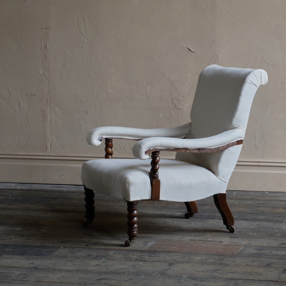 An antique open armchair upholstered in plain white calico with dark turned wooden front legs and castors.