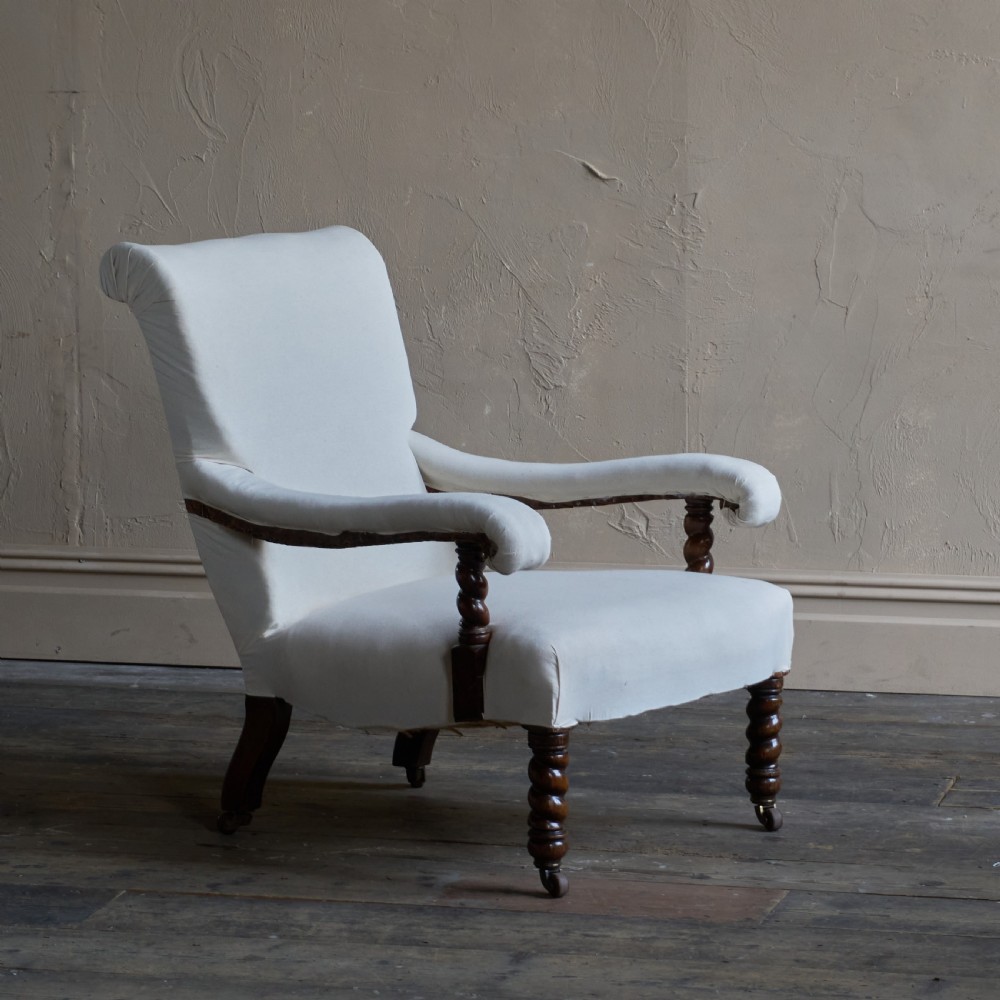 An antique open armchair upholstered in plain white calico with dark turned wooden front legs and castors. View II