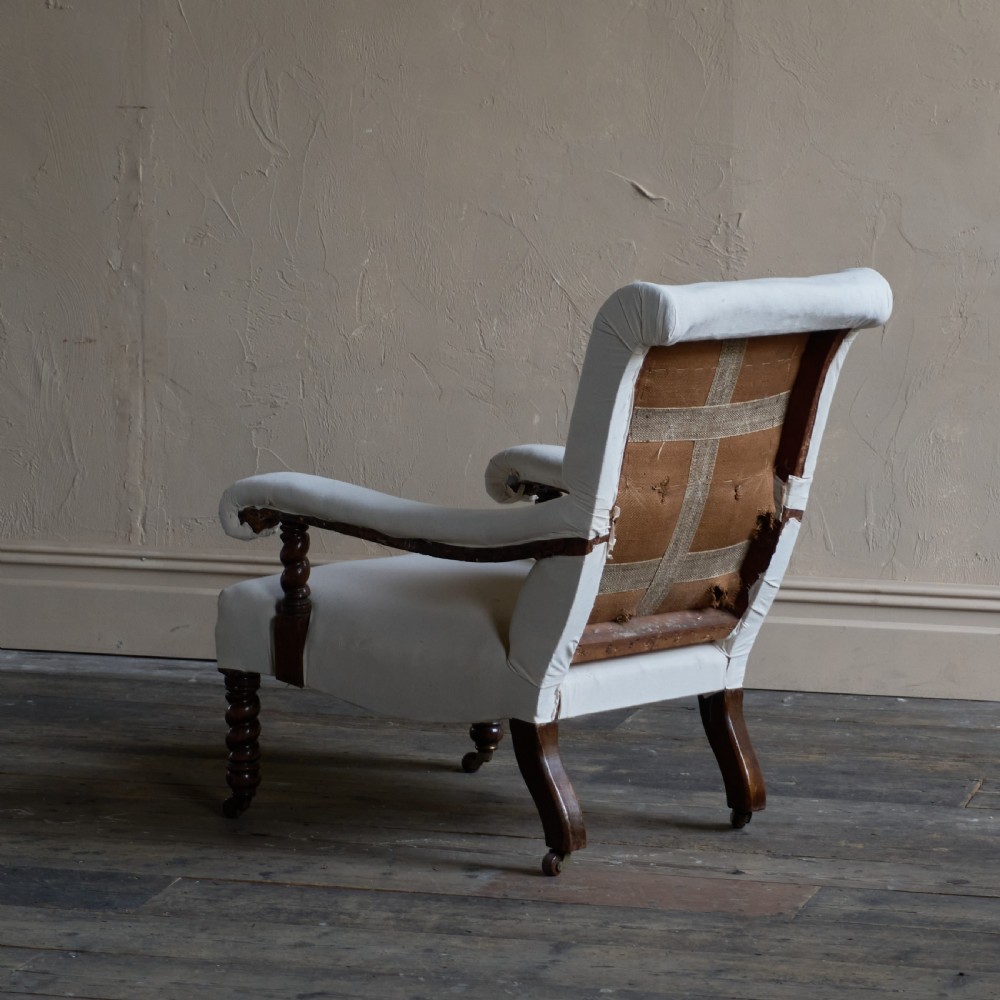 An antique open armchair upholstered in plain white calico with dark turned wooden front legs and castors. View III