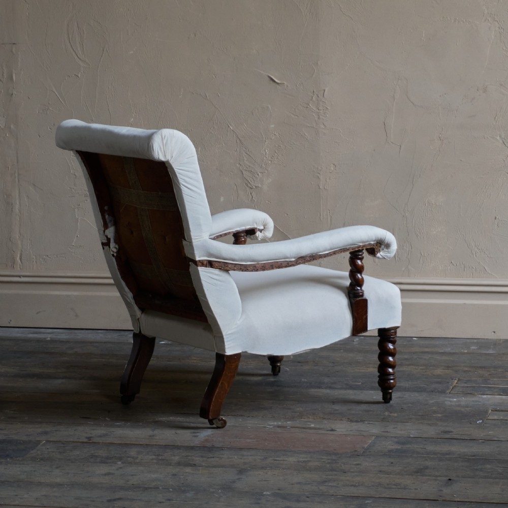 An antique open armchair upholstered in plain white calico with dark turned wooden front legs and castors. View IV