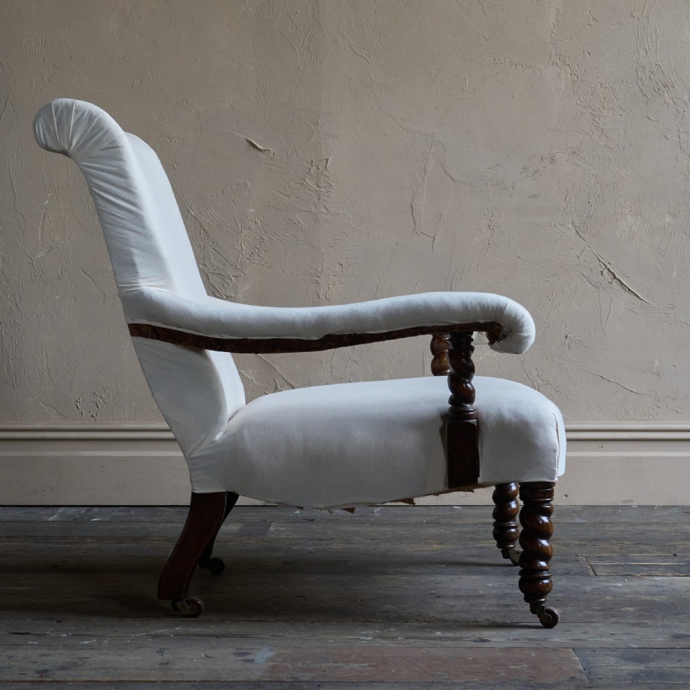 An antique open armchair upholstered in plain white calico with dark turned wooden front legs and castors. View V