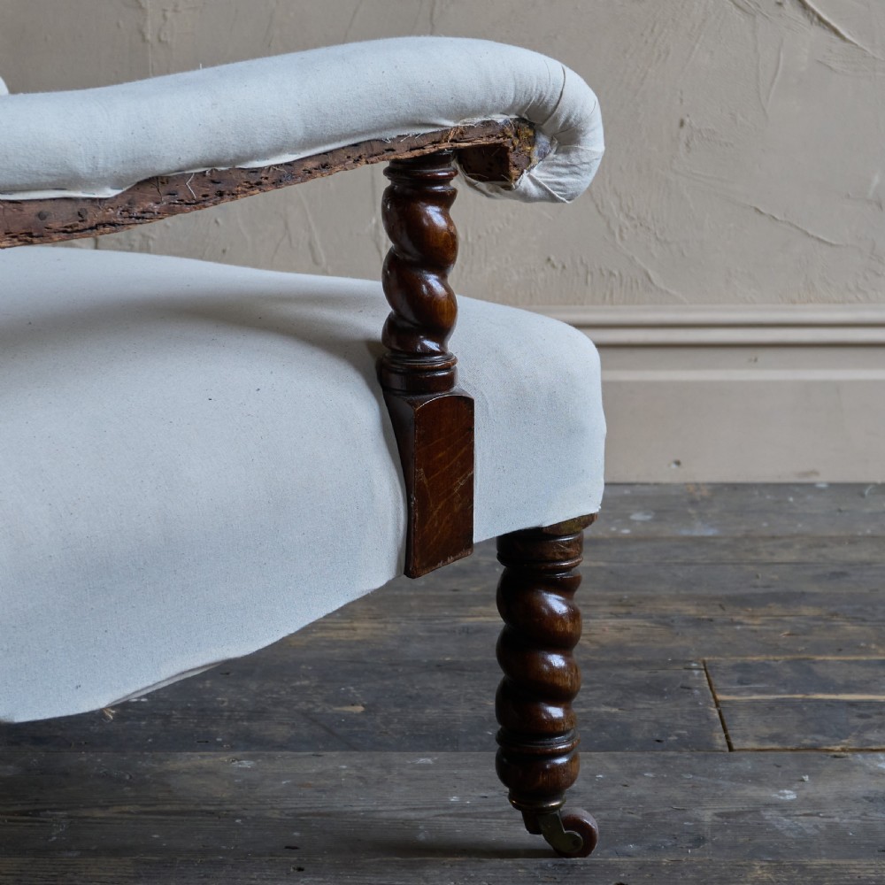 An antique open armchair upholstered in plain white calico with dark turned wooden front legs and castors. View VI