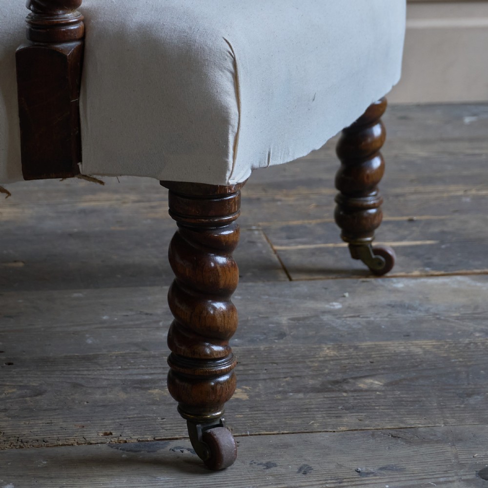 An antique open armchair upholstered in plain white calico with dark turned wooden front legs and castors. View VII