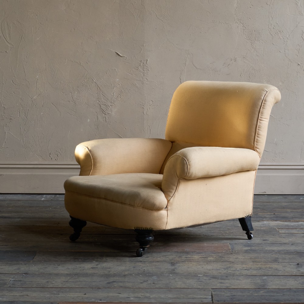 A deep-seated antique armchair with buff yellow fabric upholstery, scrolled arms, and dark turned wooden legs on castors.