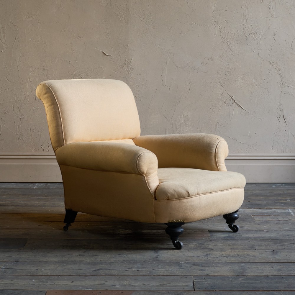 A deep-seated antique armchair with buff yellow fabric upholstery, scrolled arms, and dark turned wooden legs on castors. View II