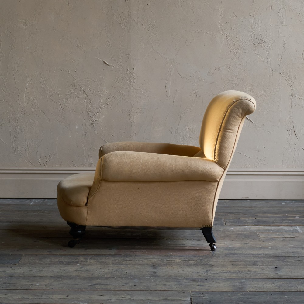 A deep-seated antique armchair with buff yellow fabric upholstery, scrolled arms, and dark turned wooden legs on castors. View V