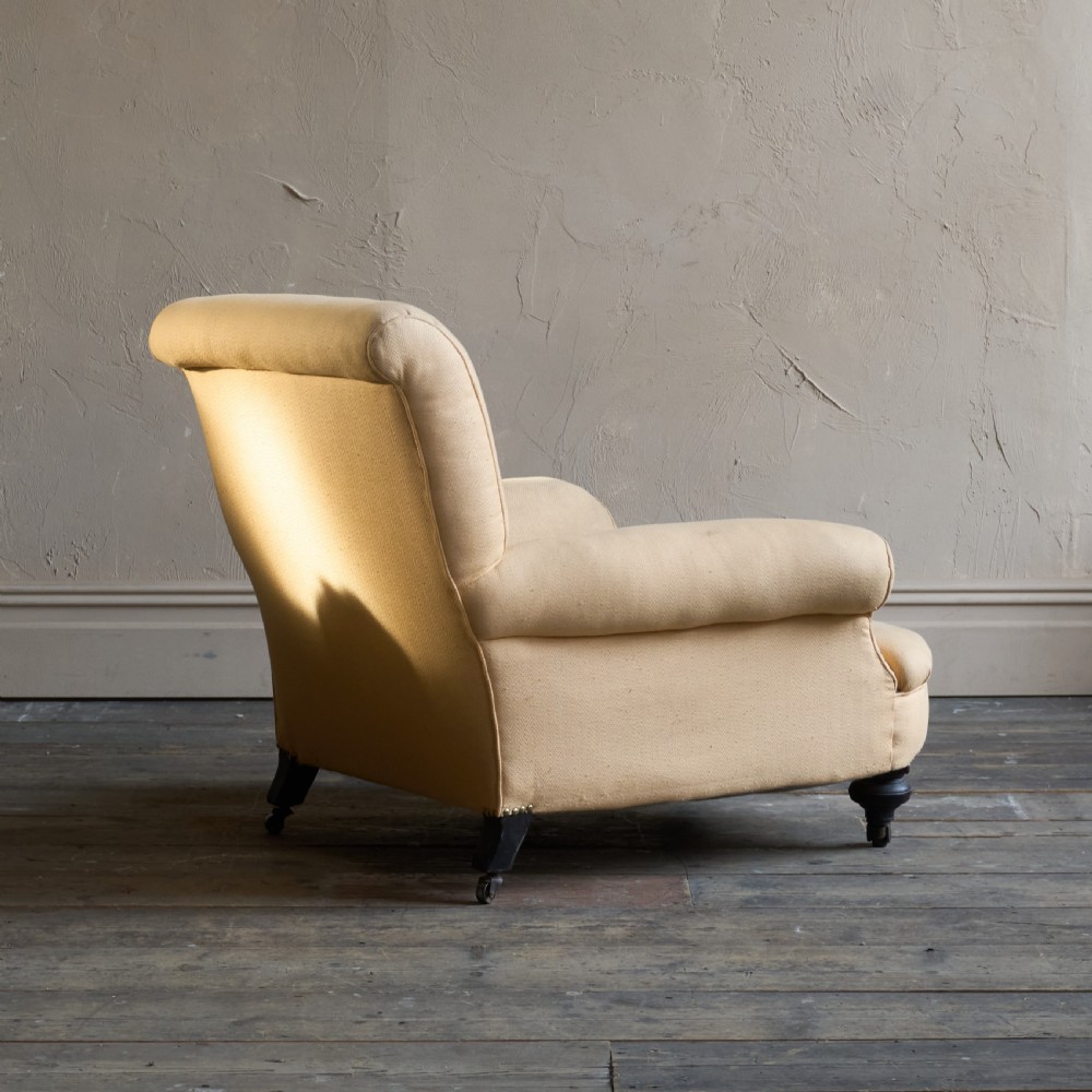 A deep-seated antique armchair with buff yellow fabric upholstery, scrolled arms, and dark turned wooden legs on castors. View VI