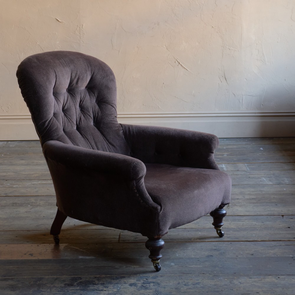 A Victorian spoon back armchair upholstered in dark brown velvet with deep button tufting on the backrest and turned wooden front legs with brass castors.
