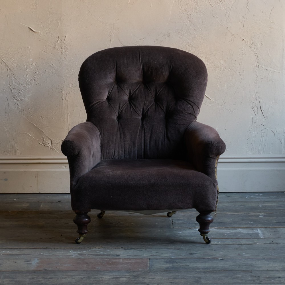 A Victorian spoon back armchair upholstered in dark brown velvet with deep button tufting on the backrest and turned wooden front legs with brass castors. View II