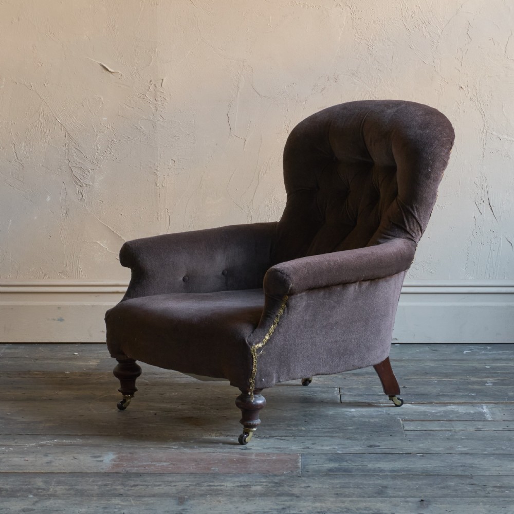 A Victorian spoon back armchair upholstered in dark brown velvet with deep button tufting on the backrest and turned wooden front legs with brass castors. View III