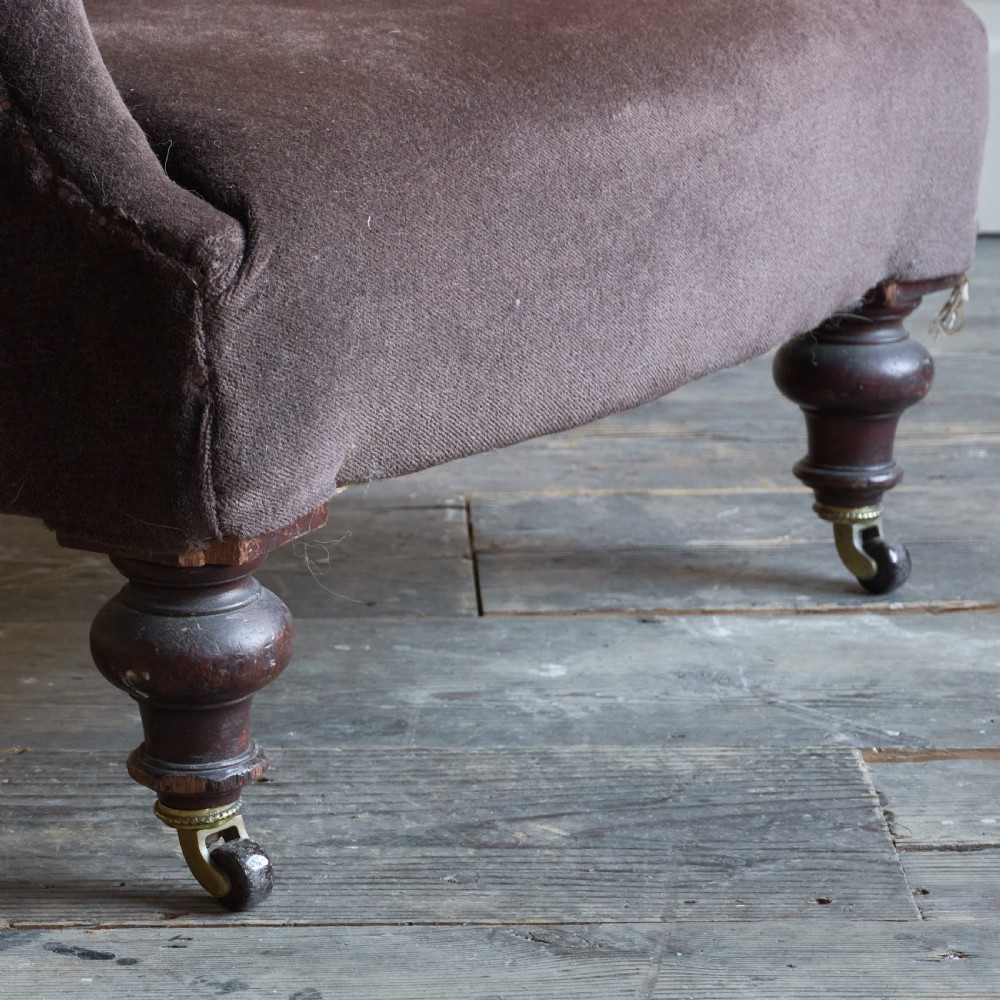 A Victorian spoon back armchair upholstered in dark brown velvet with deep button tufting on the backrest and turned wooden front legs with brass castors. View IV