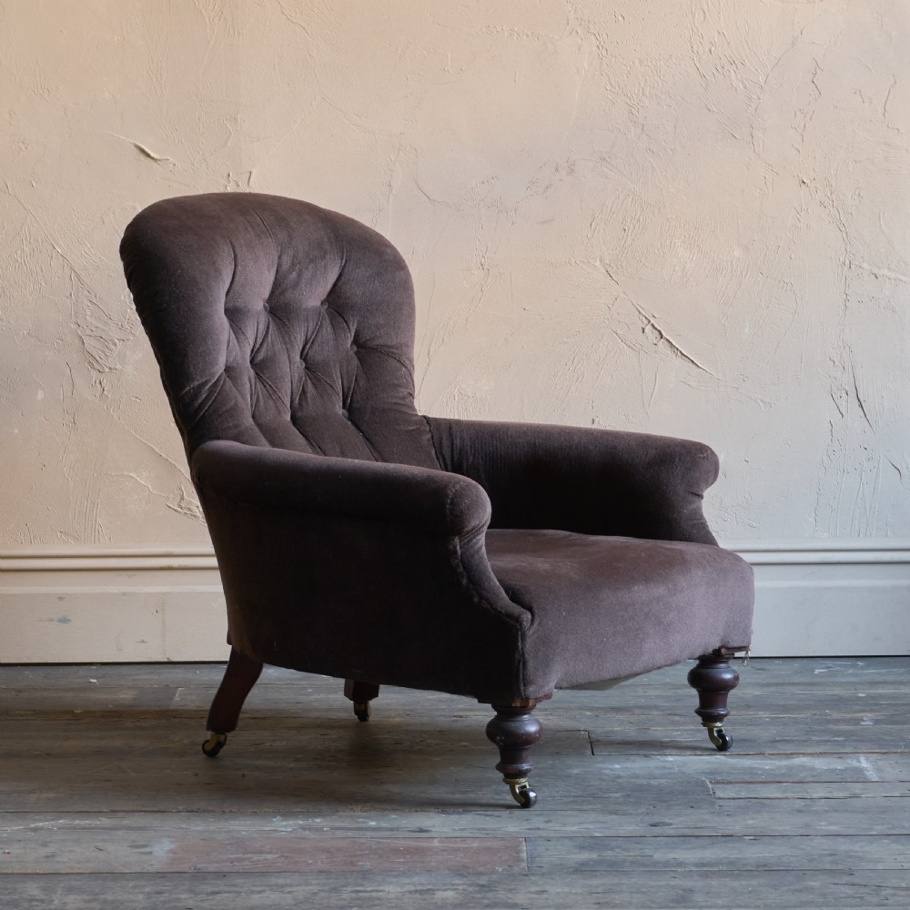 A Victorian spoon back armchair upholstered in dark brown velvet with deep button tufting on the backrest and turned wooden front legs with brass castors. View V