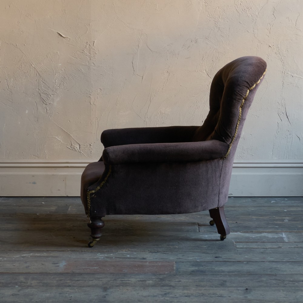 A Victorian spoon back armchair upholstered in dark brown velvet with deep button tufting on the backrest and turned wooden front legs with brass castors. View VI