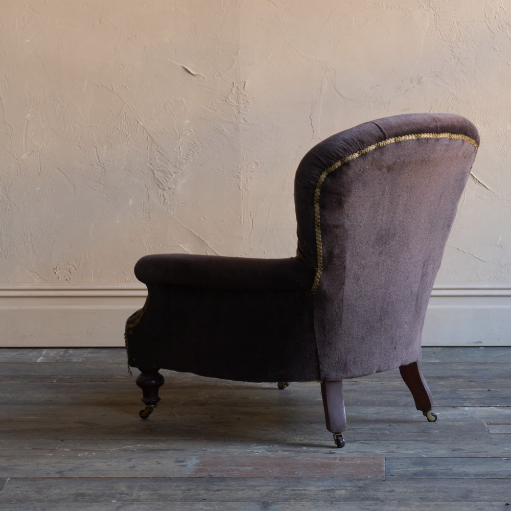 A Victorian spoon back armchair upholstered in dark brown velvet with deep button tufting on the backrest and turned wooden front legs with brass castors. View VII