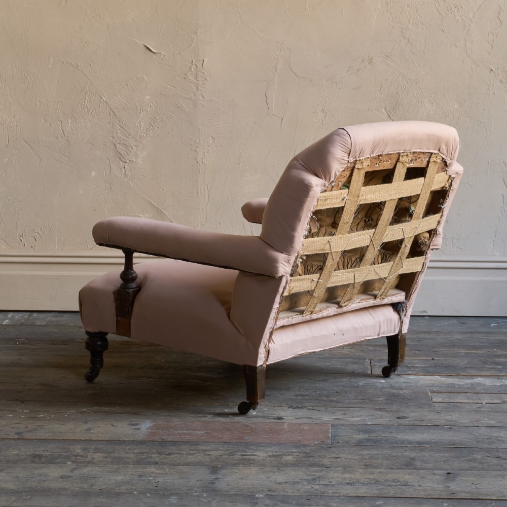 An antique upholstered armchair covered in plain beige calico fabric, featuring turned wooden legs with castors and padded armrests. View V