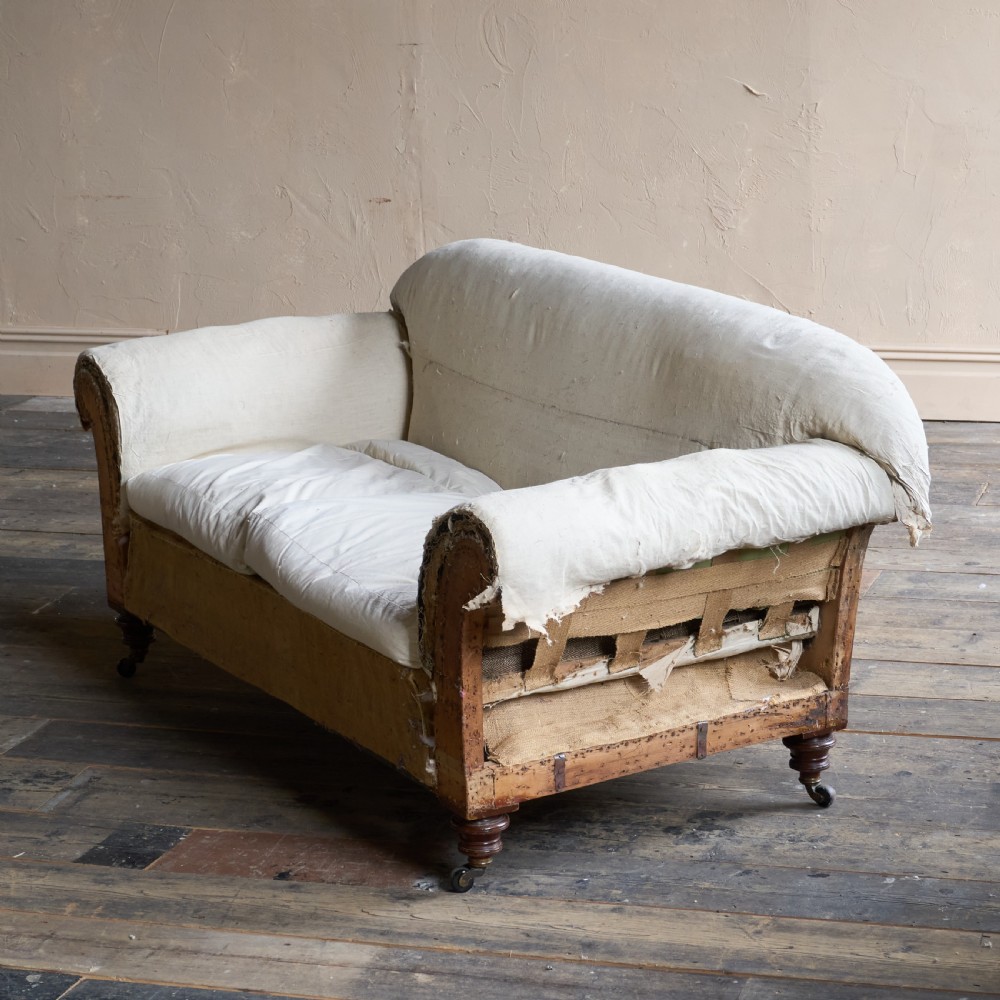 An antique two-seater country house sofa upholstered in unbleached calico with scroll arms and exposed wooden caster legs. View II