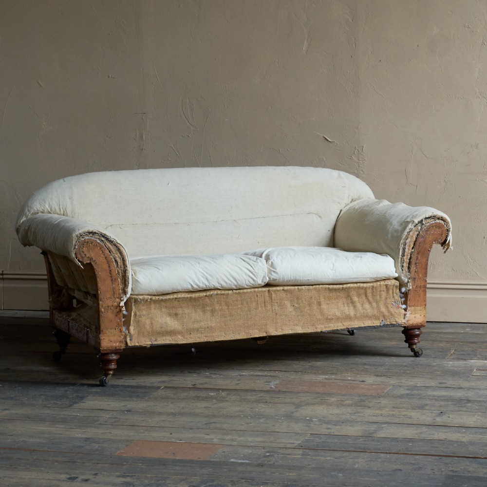 An antique two-seater country house sofa upholstered in unbleached calico with scroll arms and exposed wooden caster legs. View IV
