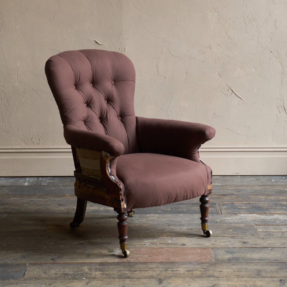 An antique Regency spoon-back armchair upholstered in dark brown fabric with button tufting and wooden castors.