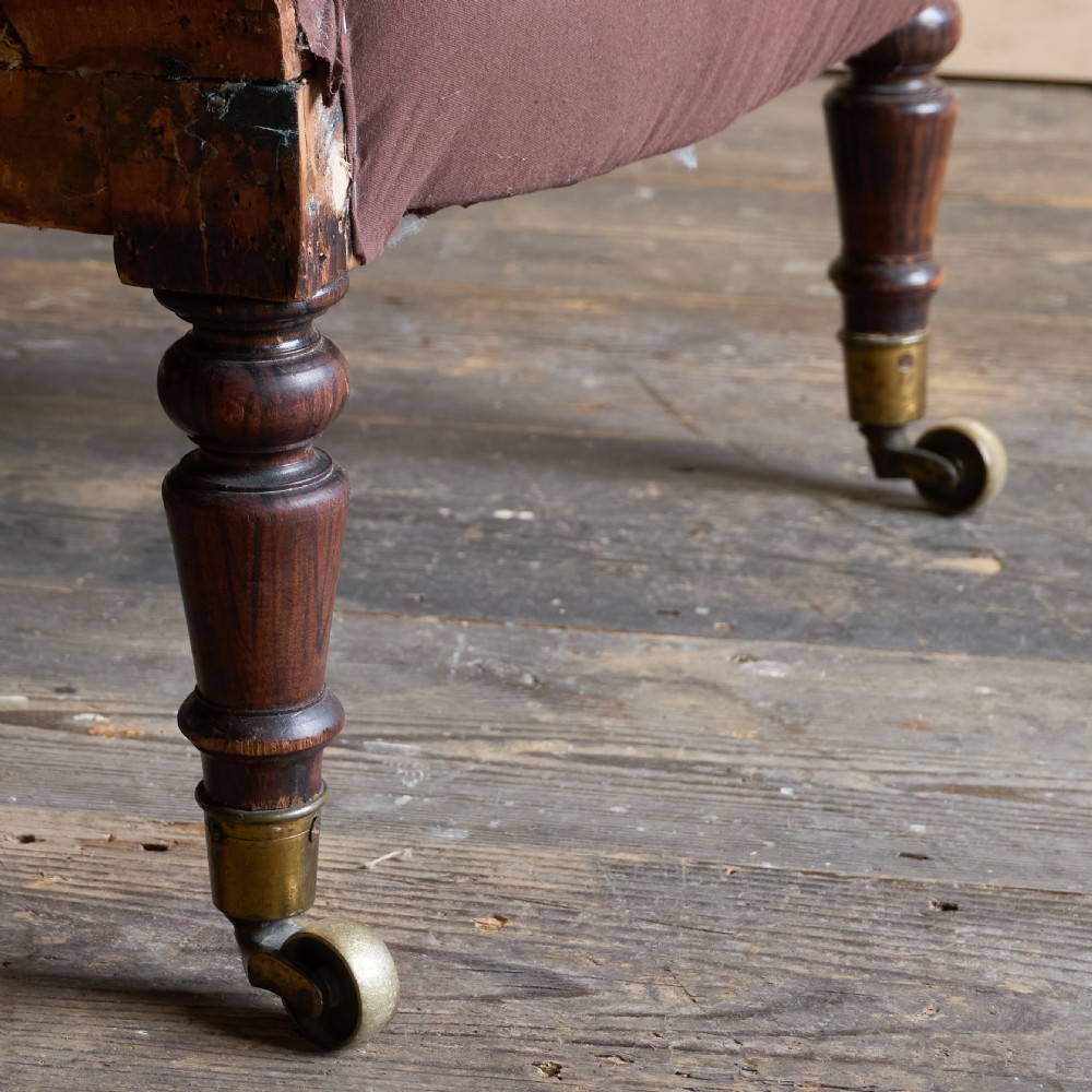 An antique Regency spoon-back armchair upholstered in dark brown fabric with button tufting and wooden castors. View V
