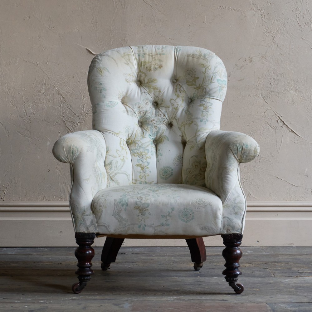 A Victorian spoon back armchair upholstered in light cream fabric with subtle floral patterns, featuring deep button tufting and turned dark wood legs on castors. View II