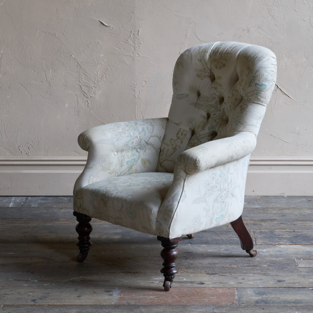 A Victorian spoon back armchair upholstered in light cream fabric with subtle floral patterns, featuring deep button tufting and turned dark wood legs on castors. View III