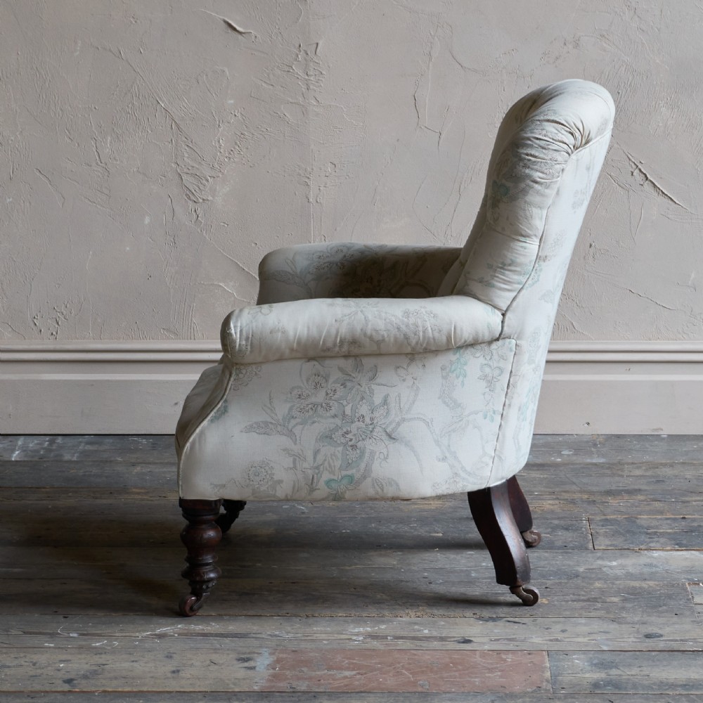 A Victorian spoon back armchair upholstered in light cream fabric with subtle floral patterns, featuring deep button tufting and turned dark wood legs on castors. View V