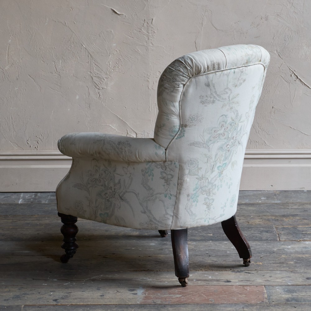 A Victorian spoon back armchair upholstered in light cream fabric with subtle floral patterns, featuring deep button tufting and turned dark wood legs on castors. View VI