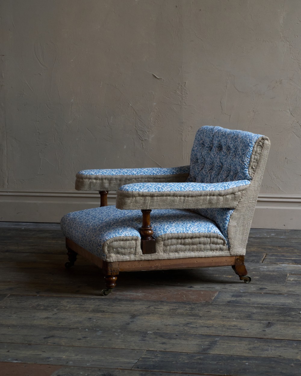 A Victorian open armchair upholstered in blue and white printed fabric with a button-tufted backrest, exposed Hessian sides, turned timber legs, and brass castors. View II