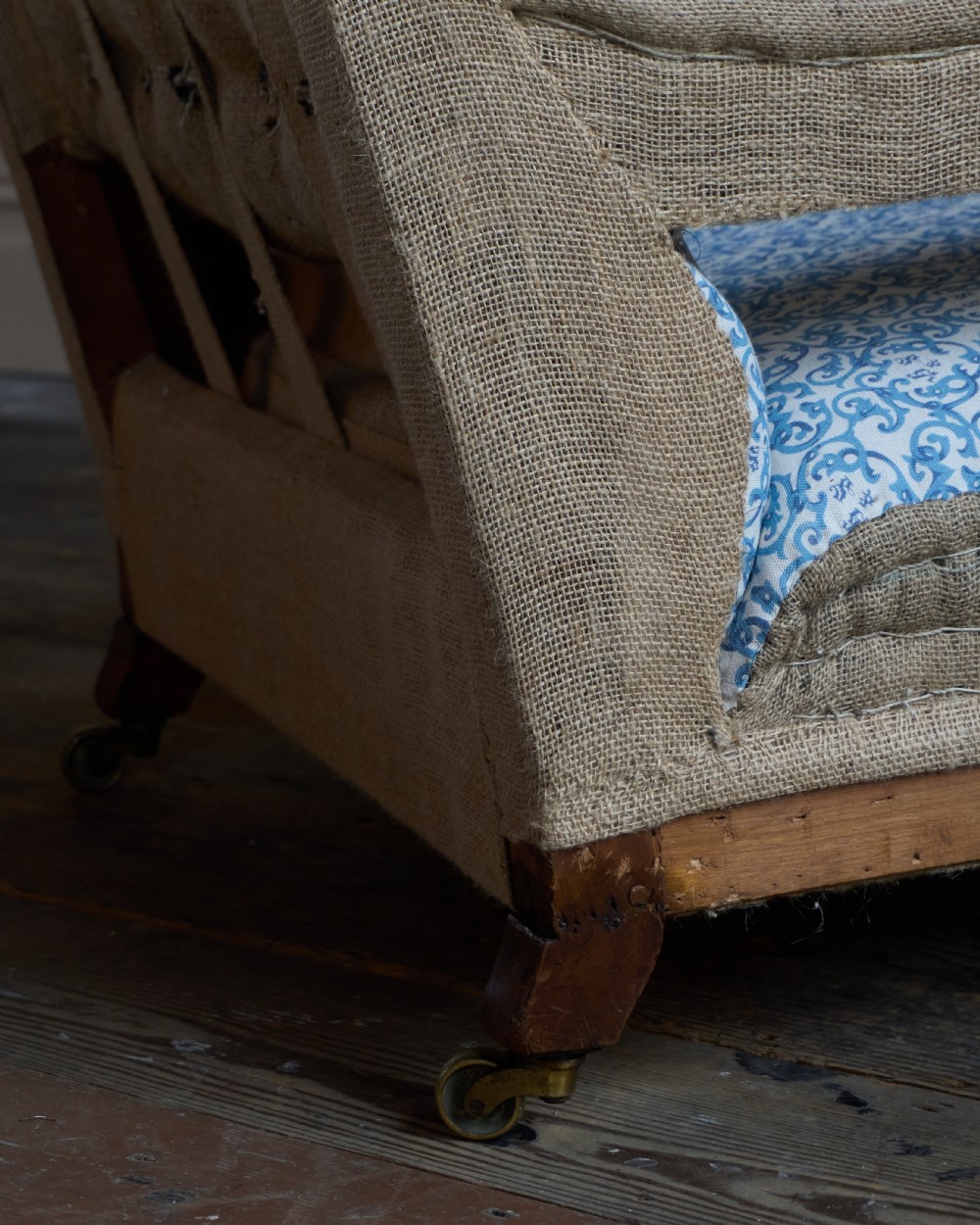 A Victorian open armchair upholstered in blue and white printed fabric with a button-tufted backrest, exposed Hessian sides, turned timber legs, and brass castors. View VII