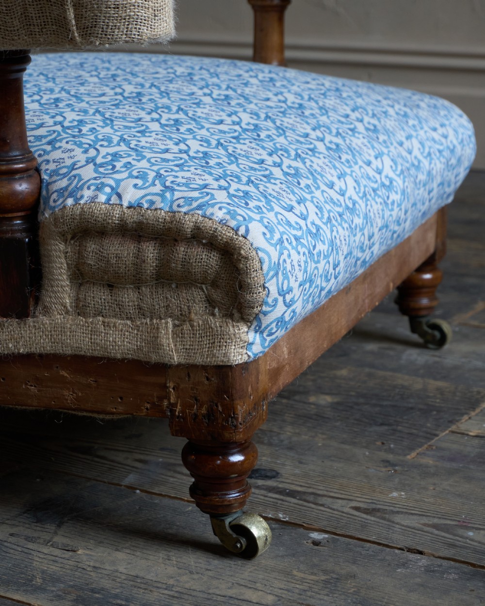 A Victorian open armchair upholstered in blue and white printed fabric with a button-tufted backrest, exposed Hessian sides, turned timber legs, and brass castors. View VIII