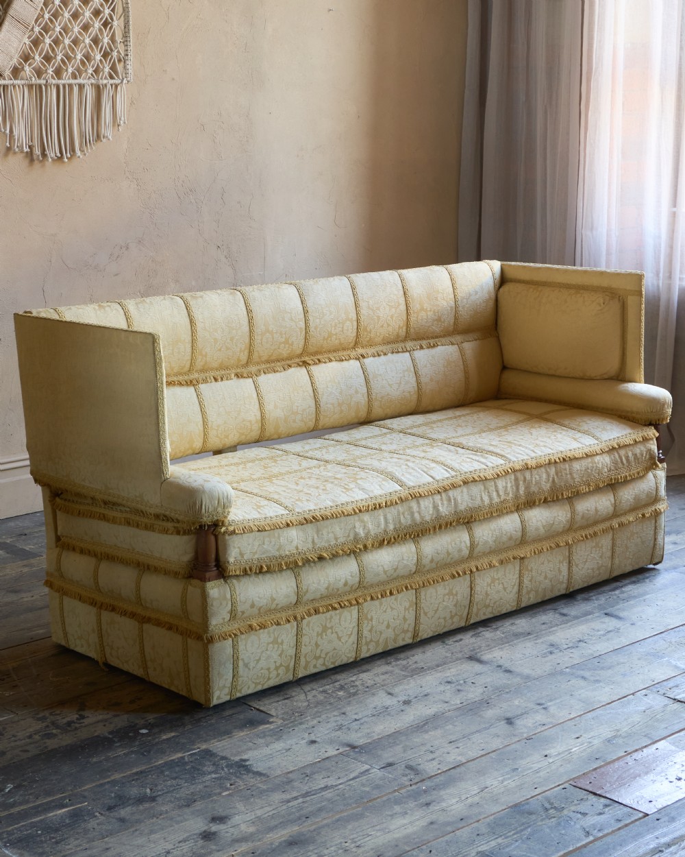 An antique gold damask Knole sofa with high drop-down side arms, fringed trim, and vertical panel upholstery.