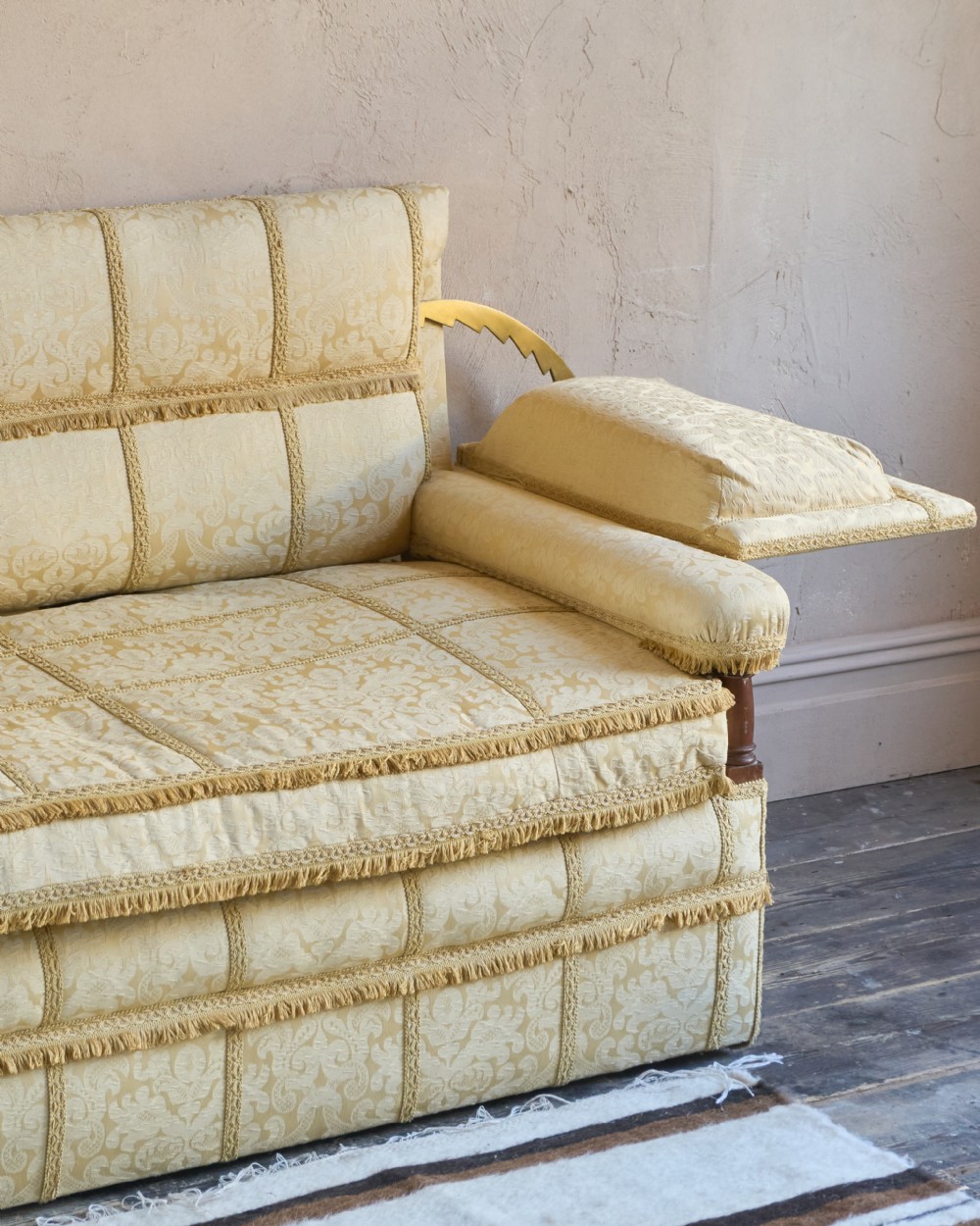 An antique gold damask Knole sofa with high drop-down side arms, fringed trim, and vertical panel upholstery. View III