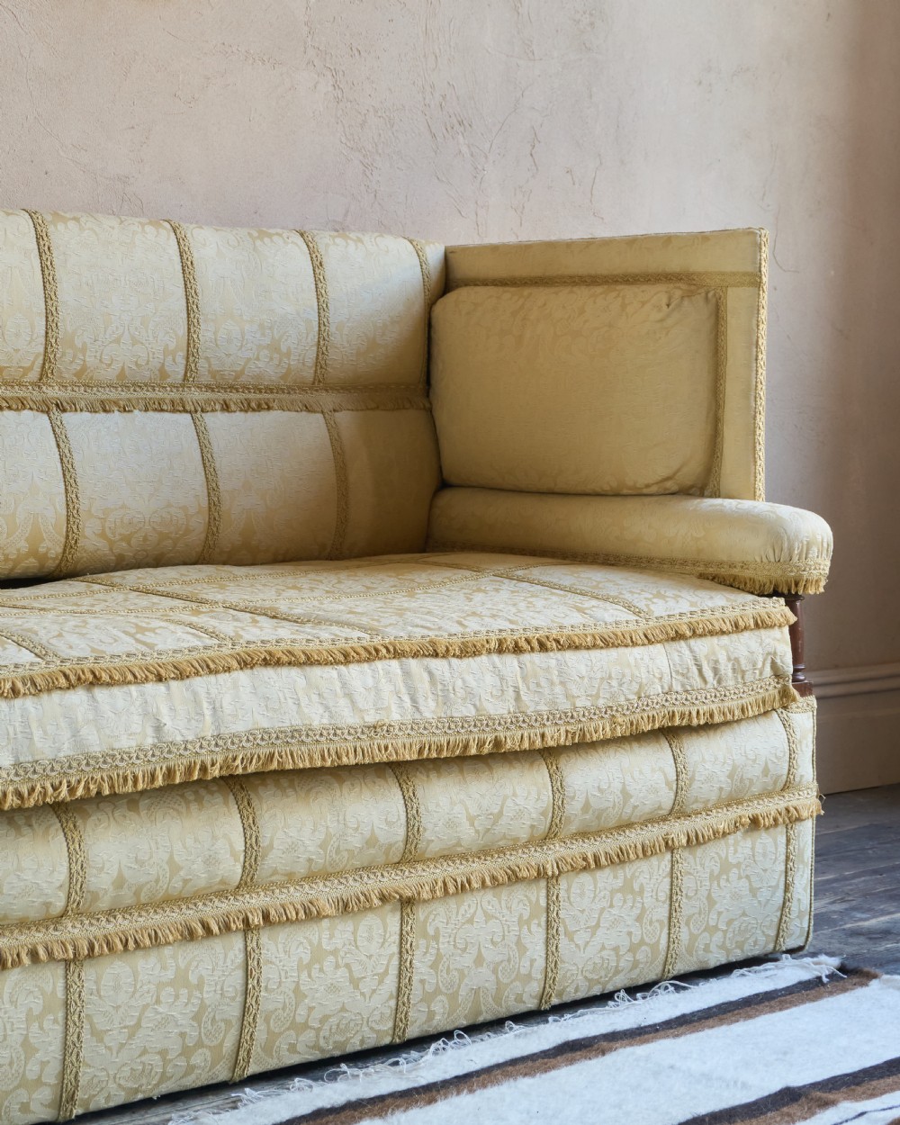 An antique gold damask Knole sofa with high drop-down side arms, fringed trim, and vertical panel upholstery. View X
