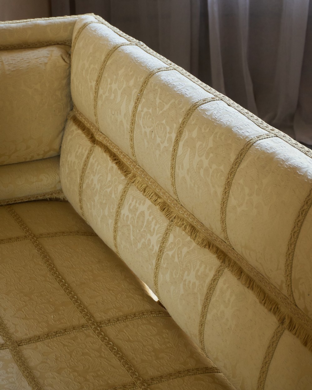 An antique gold damask Knole sofa with high drop-down side arms, fringed trim, and vertical panel upholstery. View XII