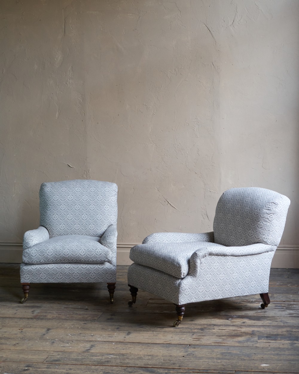 A pair of Victorian Howard and Sons Grafton style armchairs upholstered in patterned grey fabric with turned timber legs on brass castors. View II