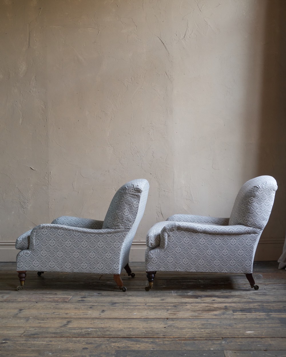 A pair of Victorian Howard and Sons Grafton style armchairs upholstered in patterned grey fabric with turned timber legs on brass castors. View IV