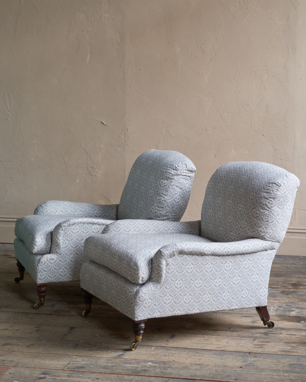 A pair of Victorian Howard and Sons Grafton style armchairs upholstered in patterned grey fabric with turned timber legs on brass castors. View VI