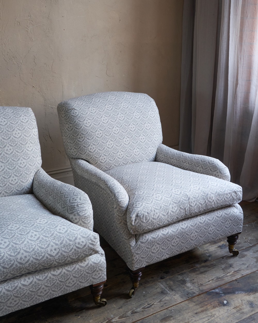 A pair of Victorian Howard and Sons Grafton style armchairs upholstered in patterned grey fabric with turned timber legs on brass castors. View X