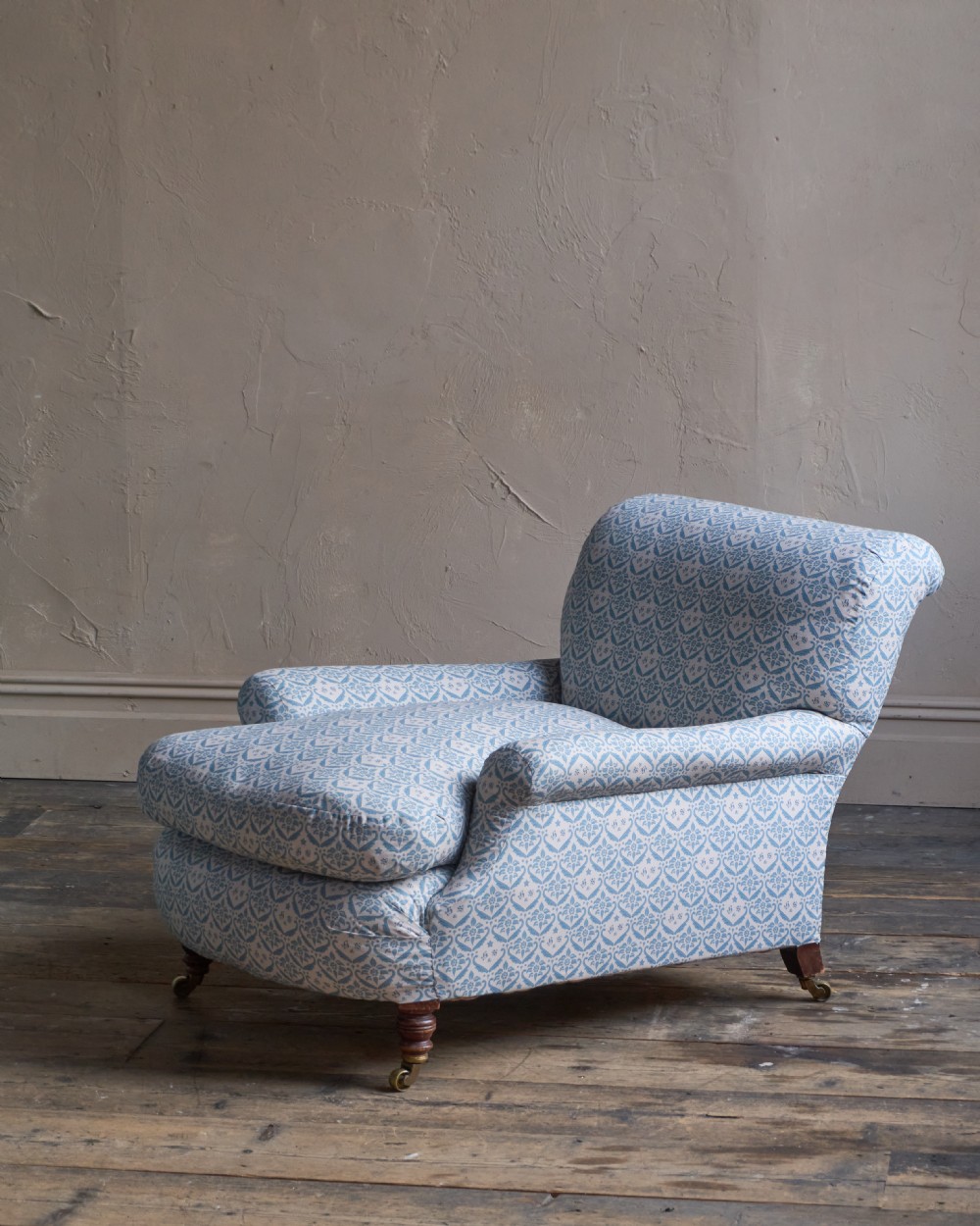 A low-slung, deeply cushioned club armchair upholstered in light blue and white patterned fabric with turned wooden legs on brass castors. View II