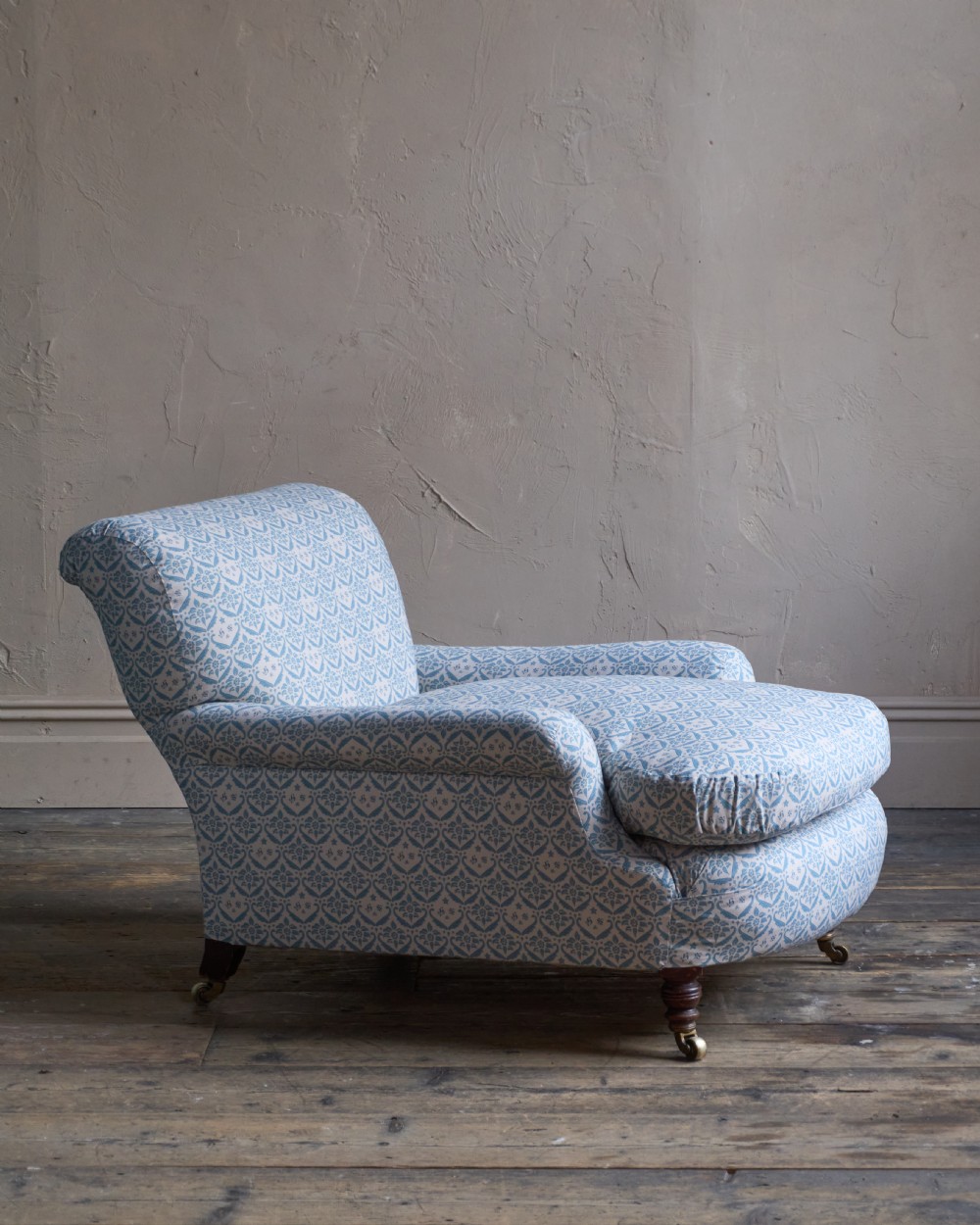 A low-slung, deeply cushioned club armchair upholstered in light blue and white patterned fabric with turned wooden legs on brass castors. View III