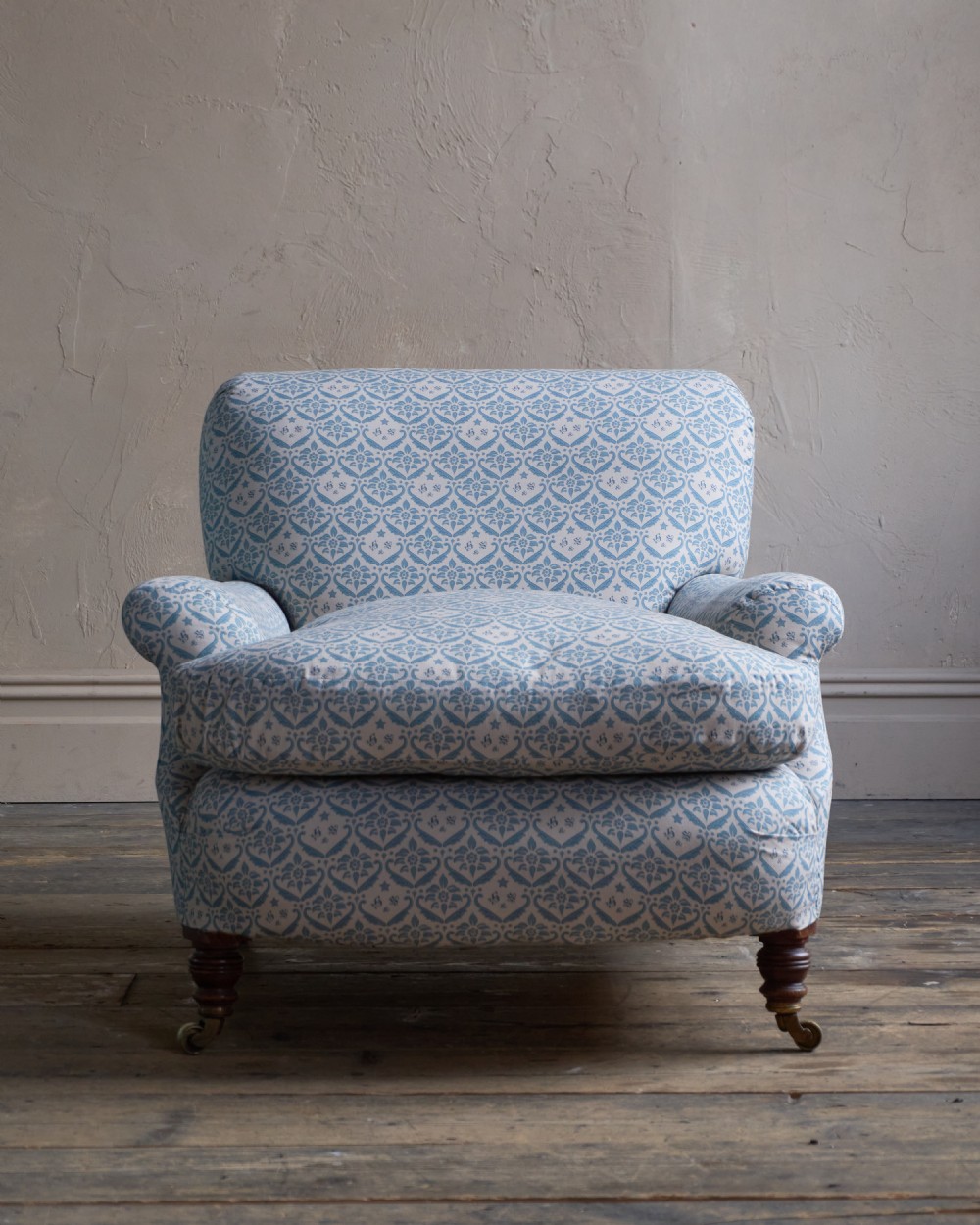 A low-slung, deeply cushioned club armchair upholstered in light blue and white patterned fabric with turned wooden legs on brass castors. View IV