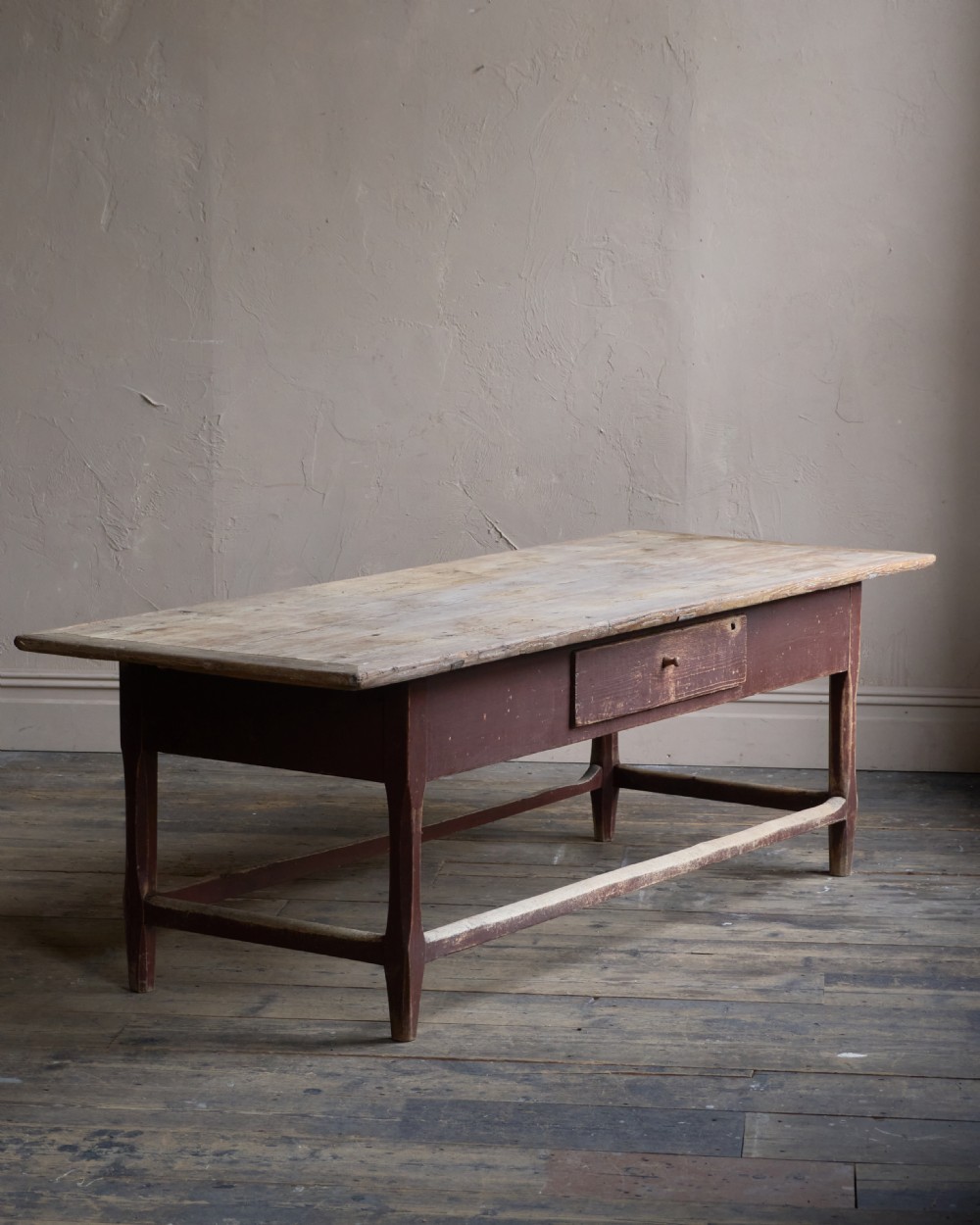 An antique Swedish kitchen table featuring an untreated scrubbed pine top, a single side drawer, and a Falu red painted apron and leg framework with stretchers.
