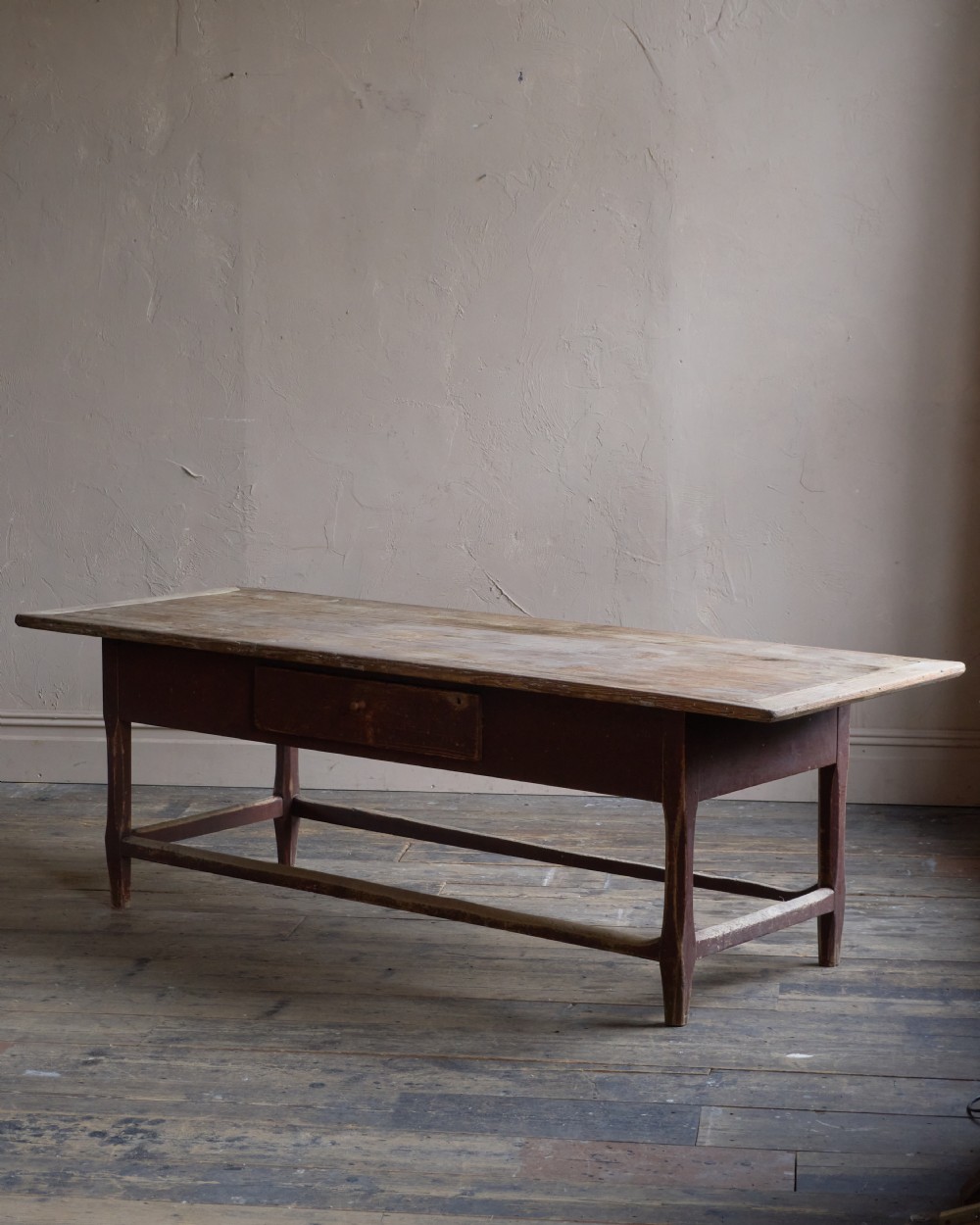 An antique Swedish kitchen table featuring an untreated scrubbed pine top, a single side drawer, and a Falu red painted apron and leg framework with stretchers. View V