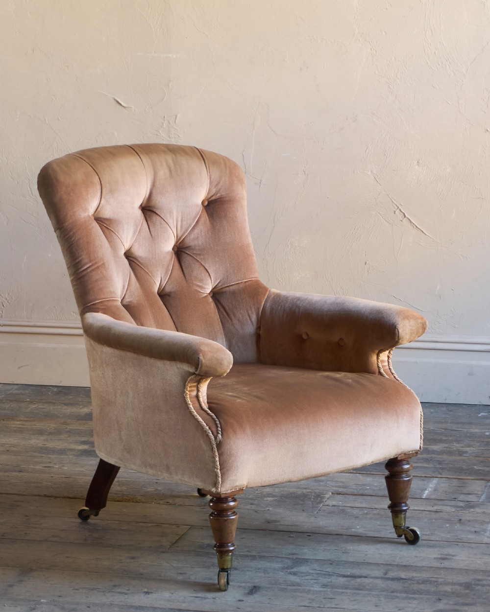 A Regency period spoon back armchair upholstered in taupe velvet with deep buttoning, turned mahogany front legs, and brass castors.