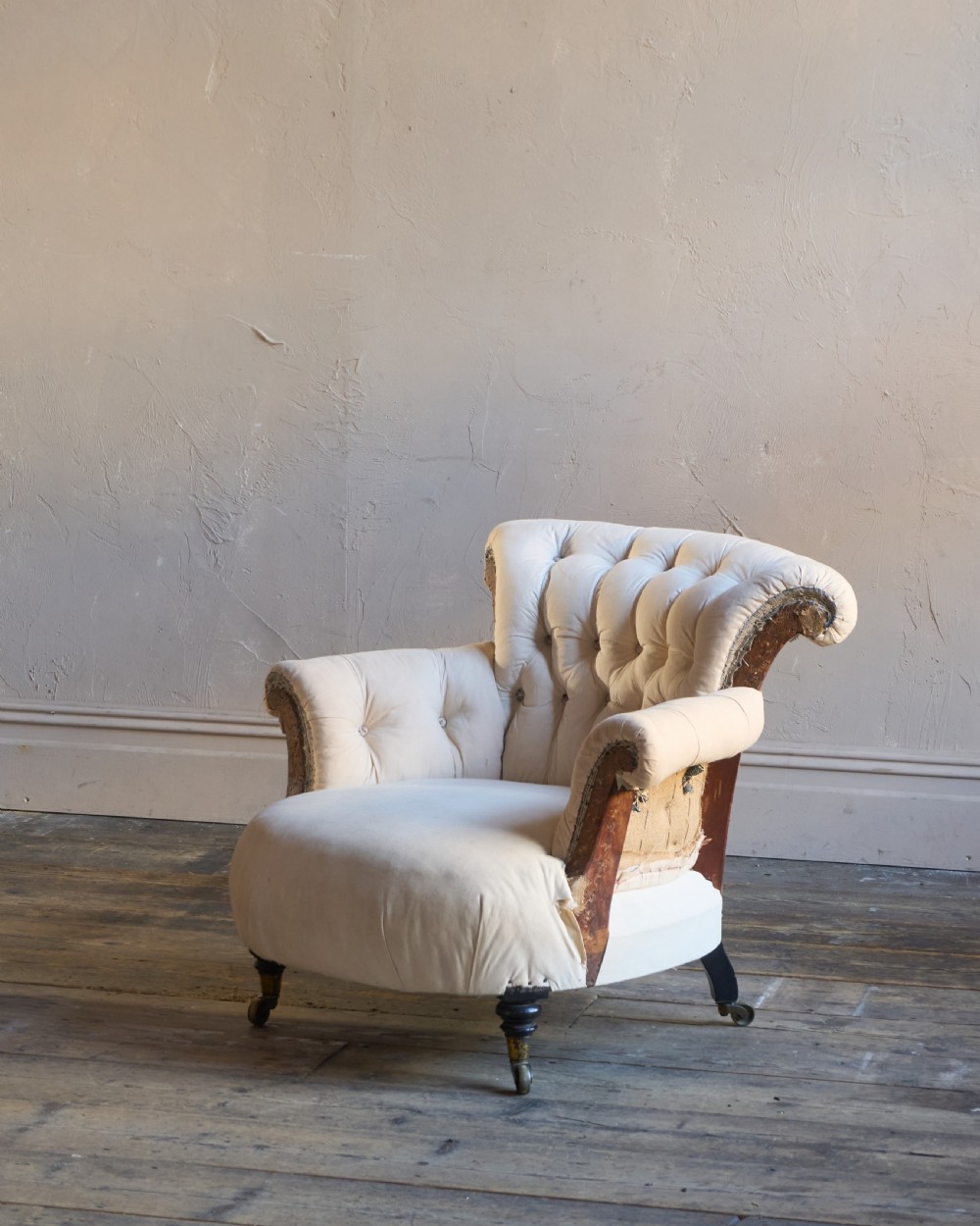 A 19th-century button-back armchair in off-white calico fabric with turned front legs resting on brass castors.