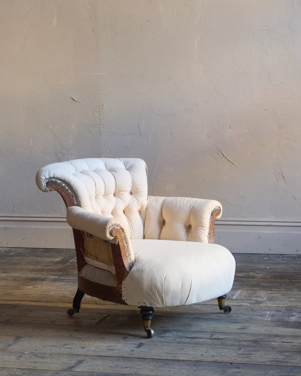 A 19th-century button-back armchair in off-white calico fabric with turned front legs resting on brass castors. View II