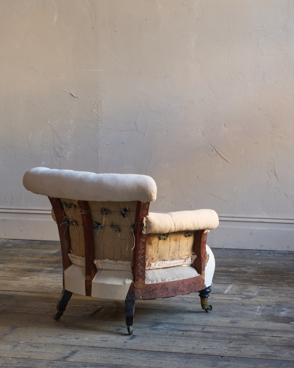A 19th-century button-back armchair in off-white calico fabric with turned front legs resting on brass castors. View IV