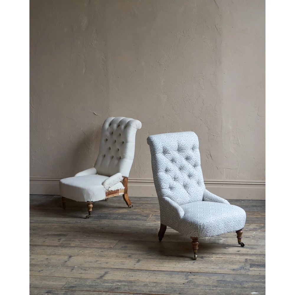 A pair of low Victorian button-back armchairs with turned wooden legs and brass castors, one in calico and one in patterned grey fabric.
