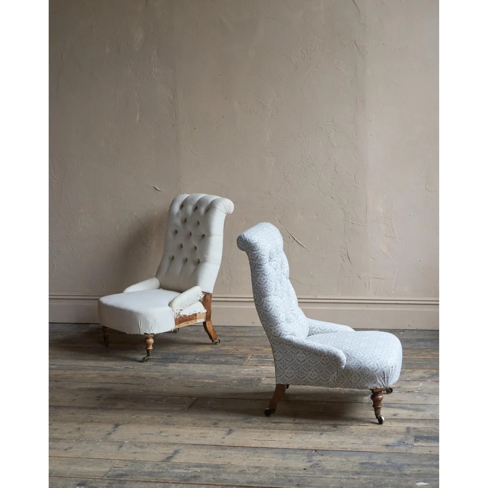 A pair of low Victorian button-back armchairs with turned wooden legs and brass castors, one in calico and one in patterned grey fabric. View II